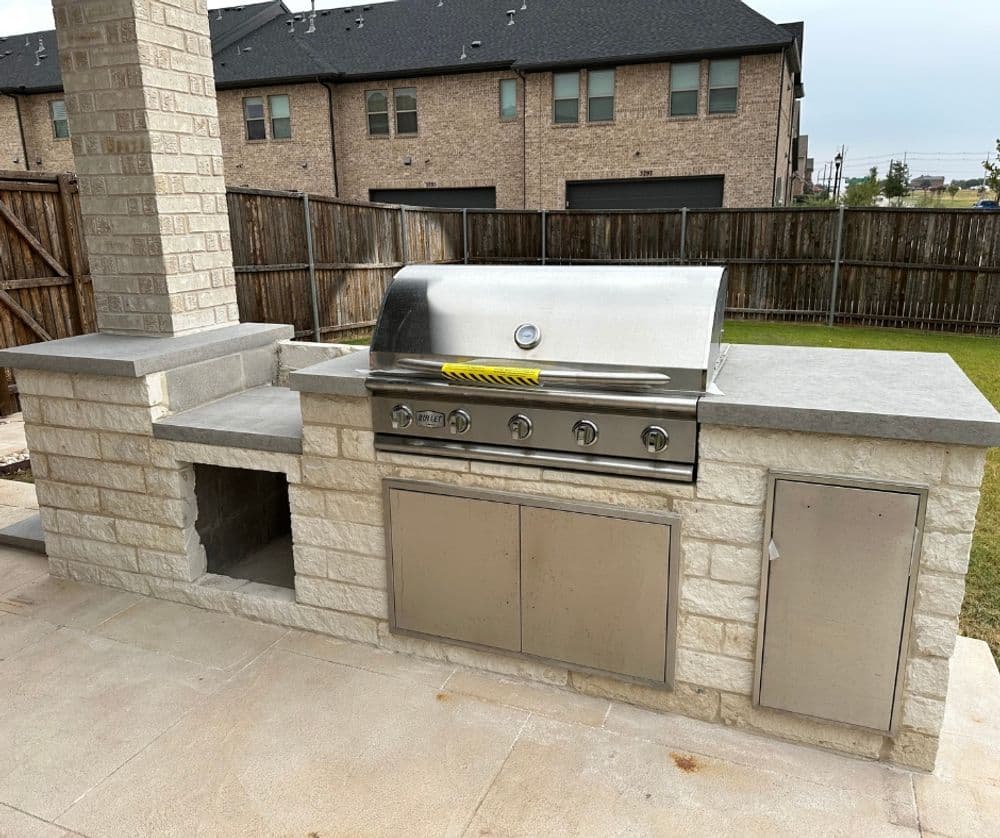 Outdoor kitchen with stainless steel grill and stone counter in a residential backyard.