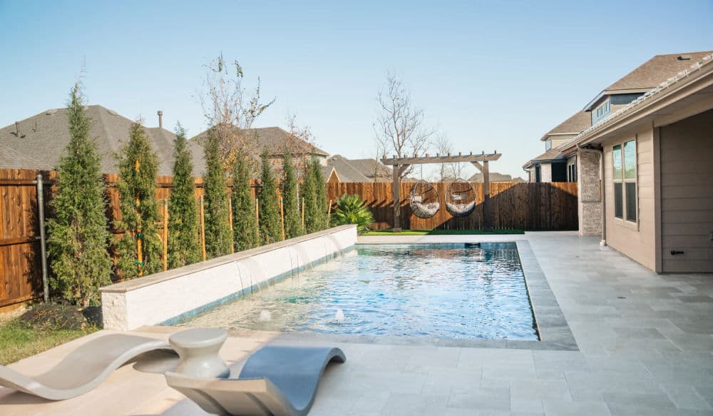 Modern backyard oasis with a pool, lounge chairs, and elegant landscaping in a sunny setting.